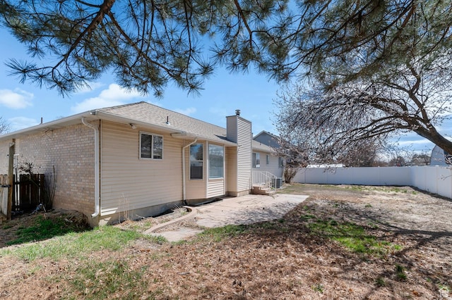 rear view of property with a fenced backyard, a chimney, a patio, and brick siding