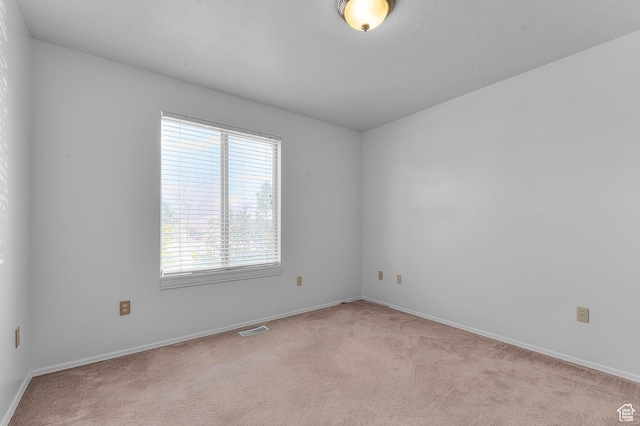 empty room featuring baseboards, visible vents, and light carpet