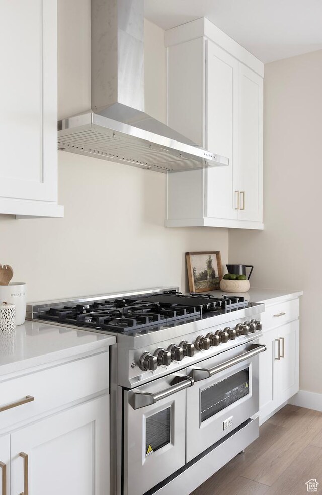 1562 E 3900 S Unit 107, Millcreek, UT 84124 - kitchen with wall chimney range hood, range with two ovens, white cabinetry, light wood finished floors, and light countertops