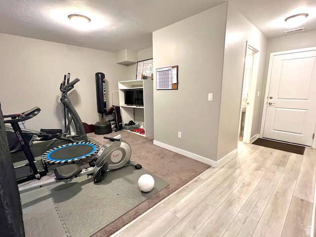 workout area featuring visible vents, baseboards, light wood finished floors, and a textured ceiling
