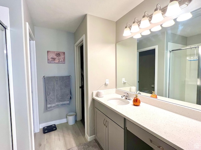 bathroom with a stall shower, toilet, vanity, wood finished floors, and baseboards