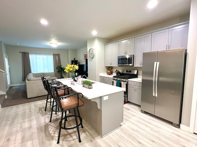 kitchen with light countertops, light wood finished floors, a breakfast bar, appliances with stainless steel finishes, and a center island with sink