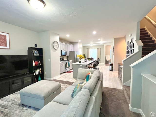 living area featuring baseboards, stairs, recessed lighting, and light colored carpet
