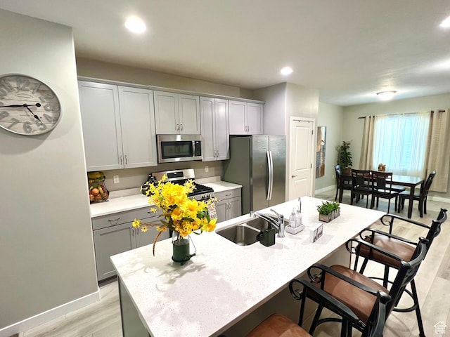 kitchen featuring light wood-style flooring, appliances with stainless steel finishes, a sink, gray cabinetry, and a kitchen breakfast bar