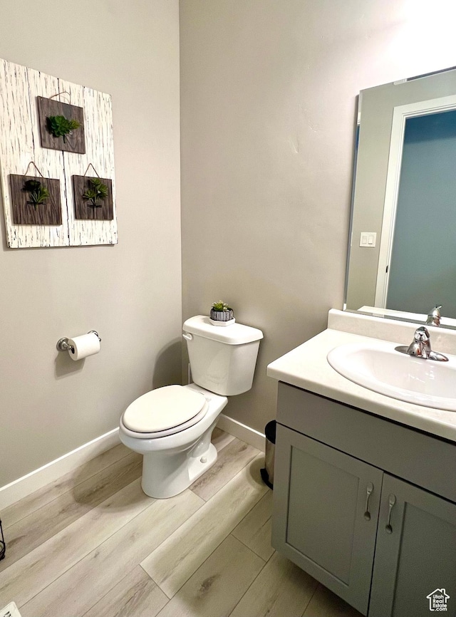 half bathroom featuring baseboards, wood finished floors, toilet, and vanity