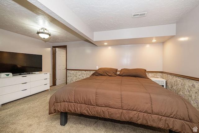 bedroom with wainscoting, carpet floors, a textured ceiling, and visible vents