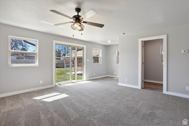 carpeted spare room featuring a ceiling fan, baseboards, a healthy amount of sunlight, and visible vents