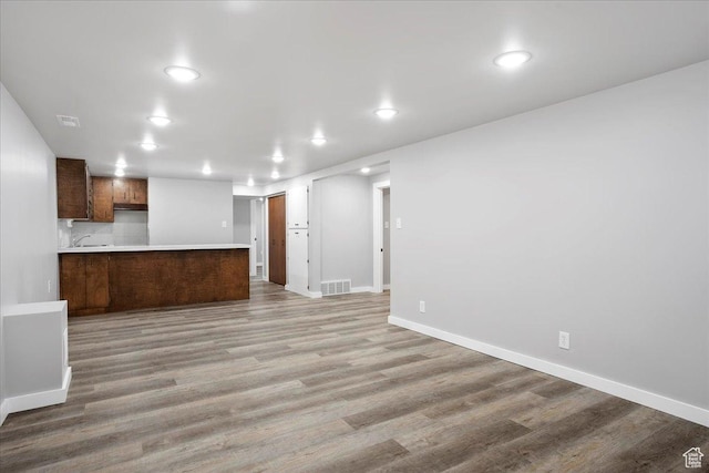 unfurnished living room with a sink, light wood-type flooring, baseboards, visible vents, and recessed lighting