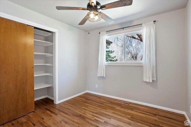 unfurnished bedroom featuring baseboards, visible vents, a closet, and wood finished floors