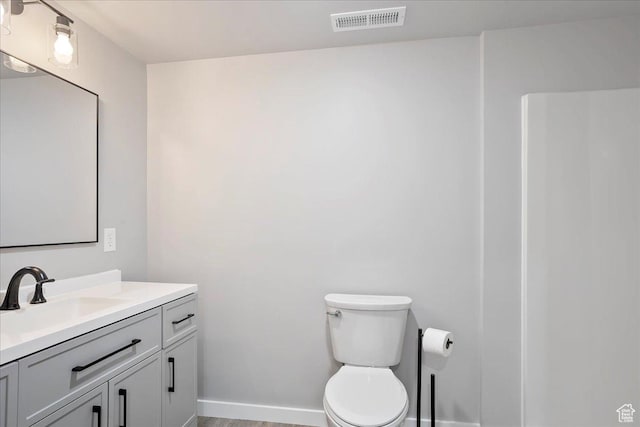 bathroom featuring visible vents, baseboards, toilet, wood finished floors, and vanity