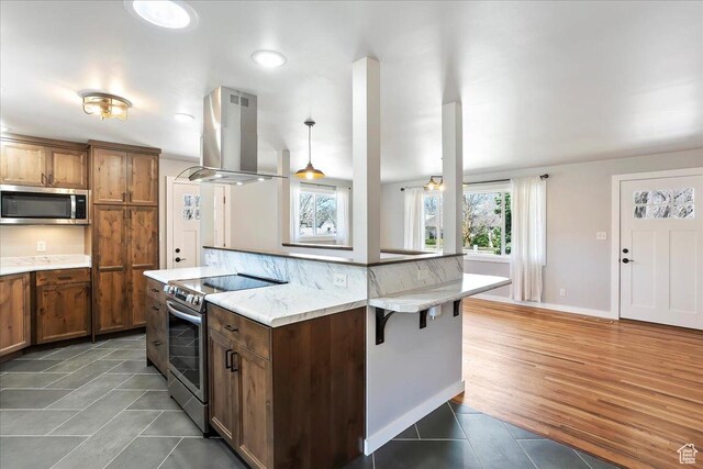 kitchen featuring island range hood, brown cabinetry, a kitchen breakfast bar, and appliances with stainless steel finishes