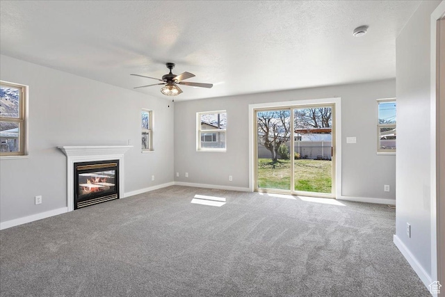 unfurnished living room with baseboards, a textured ceiling, carpet floors, a ceiling fan, and a glass covered fireplace