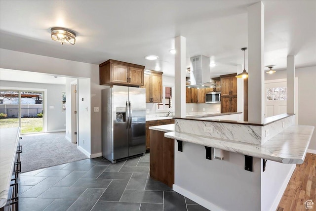 kitchen with a kitchen breakfast bar, island range hood, a peninsula, appliances with stainless steel finishes, and brown cabinetry
