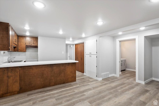 kitchen featuring light countertops, a peninsula, recessed lighting, a sink, and light wood-style floors