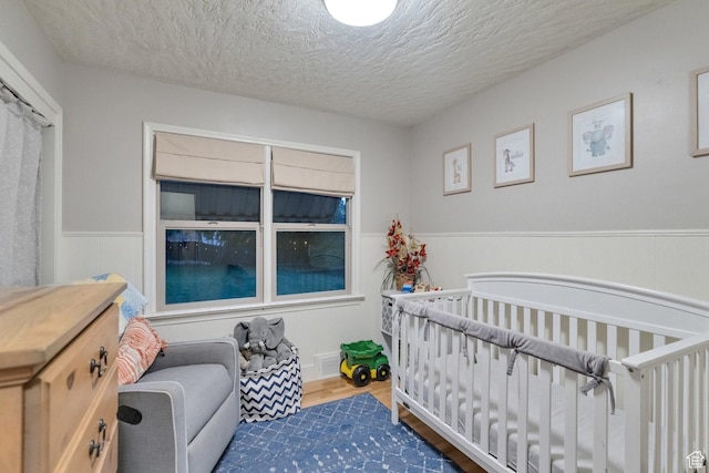 1311 E 29th St S, Ogden, UT 84403 - bedroom with a nursery area, a textured ceiling, a wainscoted wall, visible vents, and wood finished floors