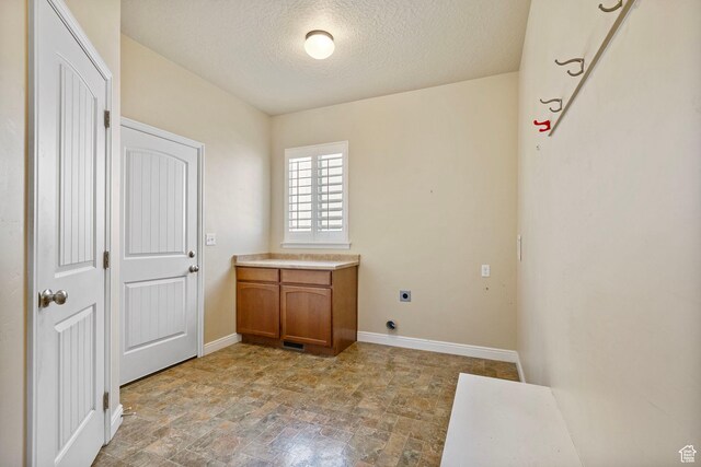 laundry area with a textured ceiling, stone finish flooring, baseboards, hookup for an electric dryer, and cabinet space