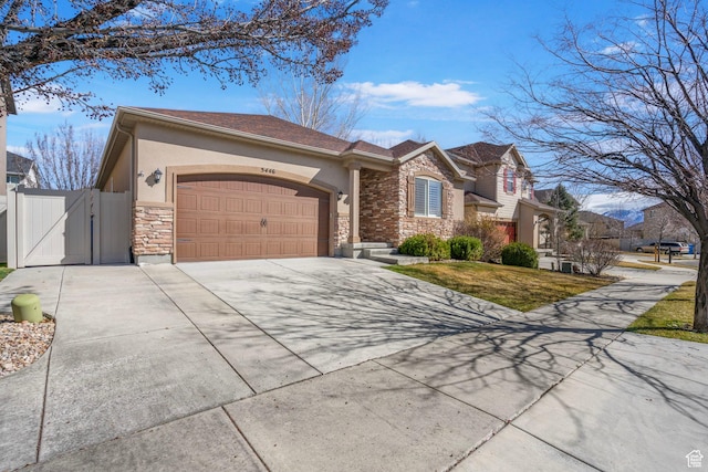 view of front facade with stone siding, a gate, an attached garage, concrete driveway, and stucco siding