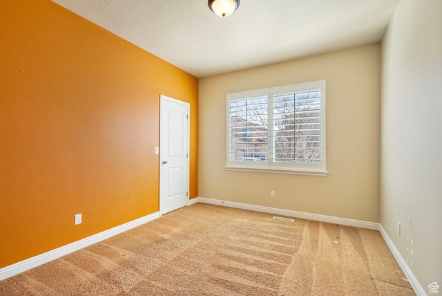 empty room with baseboards, a textured ceiling, visible vents, and carpet