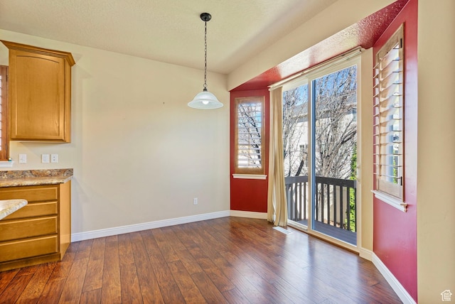 unfurnished dining area with baseboards, dark wood-style flooring, and a textured ceiling