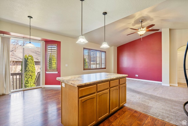 kitchen with light countertops, a ceiling fan, hanging light fixtures, brown cabinetry, and dark wood-style flooring