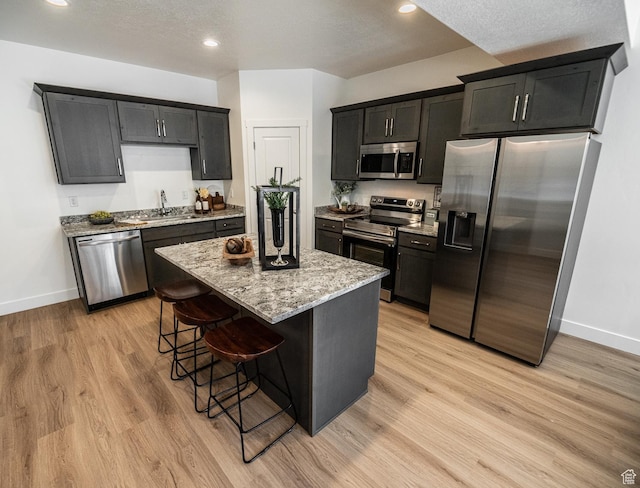 kitchen featuring a kitchen island, appliances with stainless steel finishes, light stone countertops, baseboards, and a breakfast bar