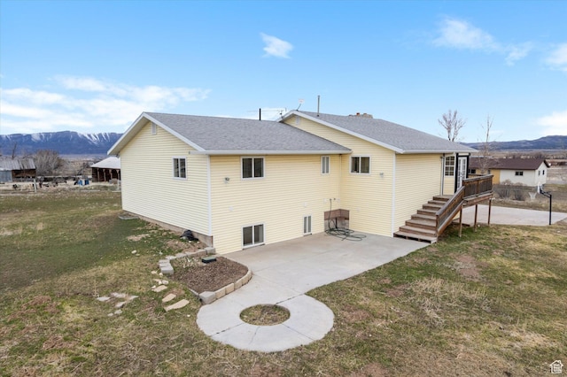 back of house with roof with shingles, a mountain view, a yard, and a patio