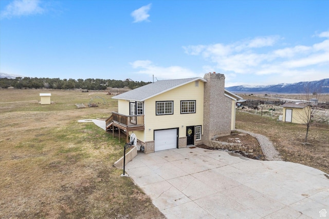 view of side of home featuring a chimney, a garage, concrete driveway, a mountain view, and a yard