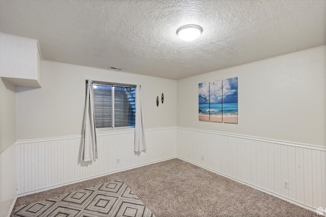 unfurnished room featuring a wainscoted wall, a textured ceiling, visible vents, and carpet