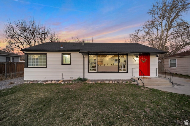 ranch-style home with entry steps, fence, roof with shingles, and a yard