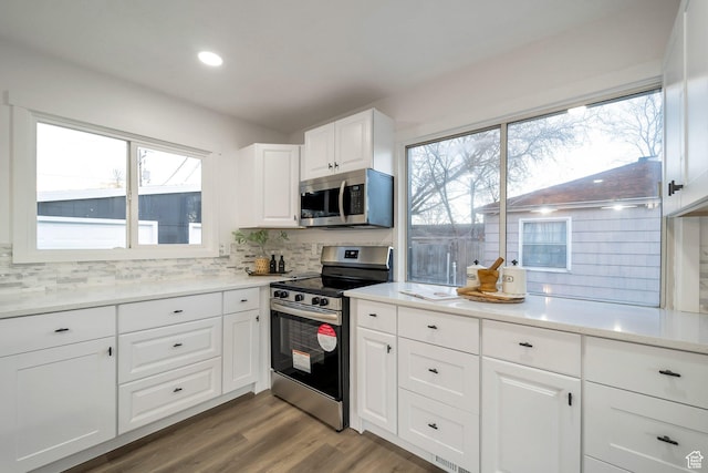 kitchen with light countertops, tasteful backsplash, wood finished floors, stainless steel appliances, and white cabinets