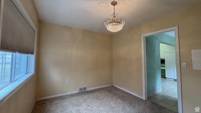 carpeted empty room featuring a chandelier and baseboards