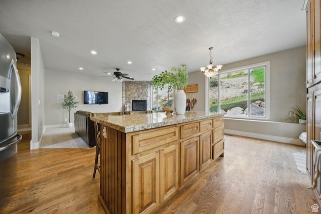 1637 E 2400 N, Layton, UT 84040 - kitchen with light wood finished floors, a kitchen island, a stone fireplace, ceiling fan with notable chandelier, and stainless steel fridge with ice dispenser