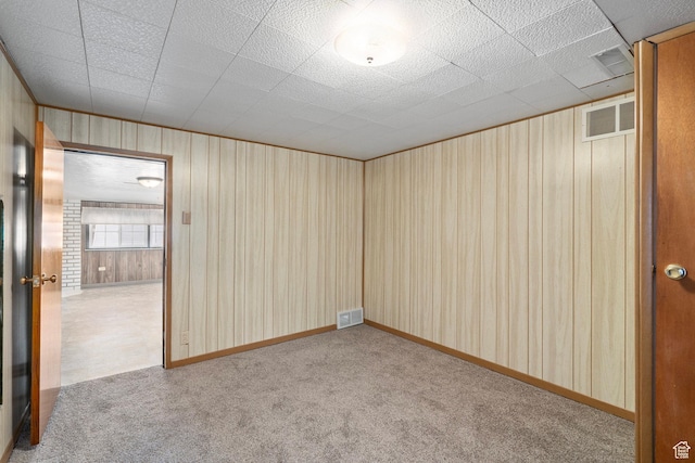 empty room with visible vents, wooden walls, and carpet flooring