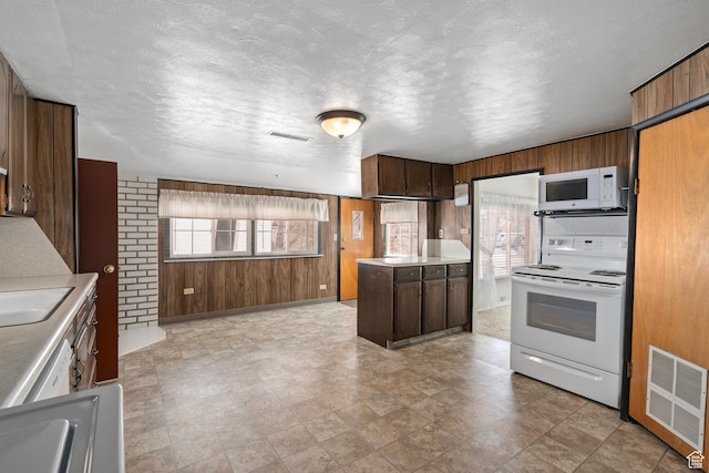 kitchen with a textured ceiling, wood walls, light countertops, visible vents, and white appliances