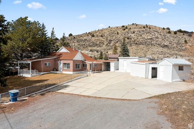 view of front of property with fence, a storage shed, concrete driveway, brick siding, and an outdoor structure