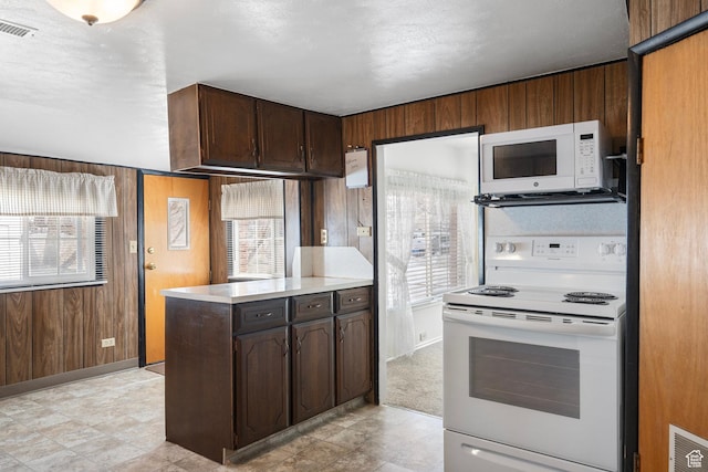 kitchen with light countertops, visible vents, wooden walls, and white appliances
