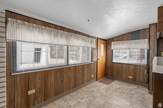 spare room featuring wooden walls, lofted ceiling, and a textured ceiling
