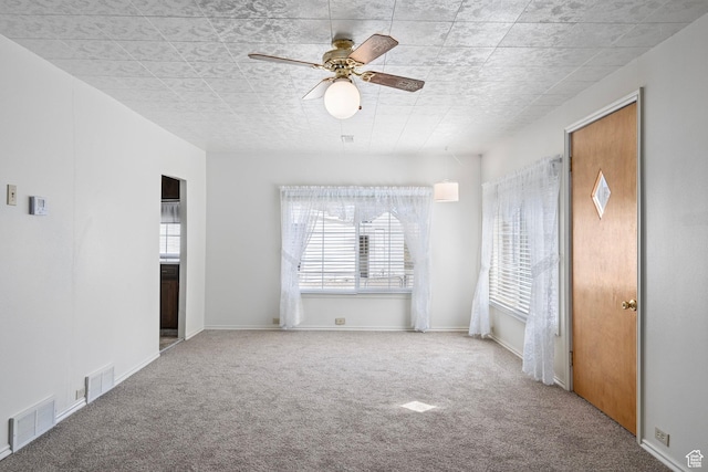 carpeted spare room with baseboards, ceiling fan, and visible vents