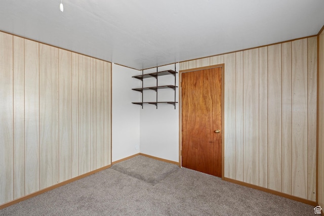 carpeted empty room with baseboards and wood walls