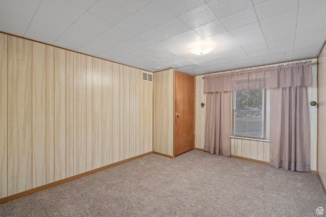 carpeted empty room with visible vents and wood walls