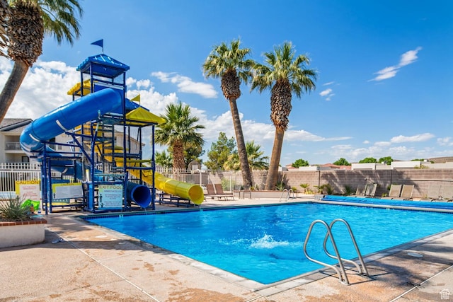 community pool featuring a water slide, playground community, and fence