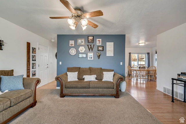 living area with baseboards, ceiling fan, visible vents, and wood finished floors