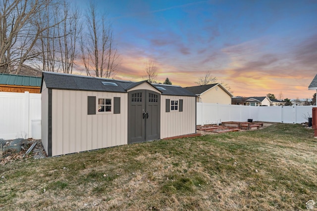 outdoor structure at dusk featuring a fenced backyard, a yard, and a storage shed