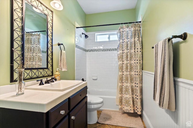 full bath with tile patterned flooring, vanity, shower / tub combo, toilet, and wainscoting