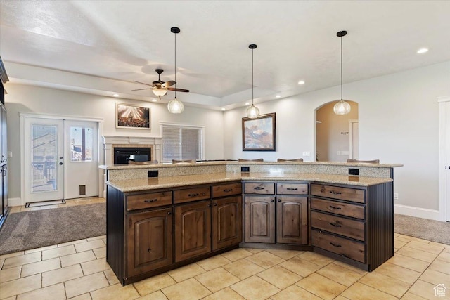 kitchen featuring a ceiling fan, a glass covered fireplace, open floor plan, arched walkways, and dark brown cabinets