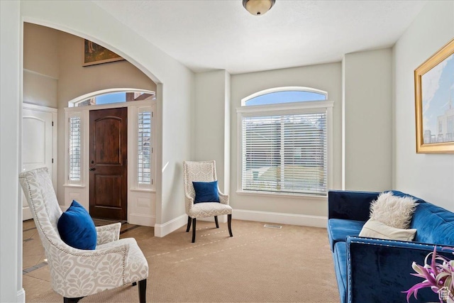 sitting room featuring arched walkways, baseboards, and carpet