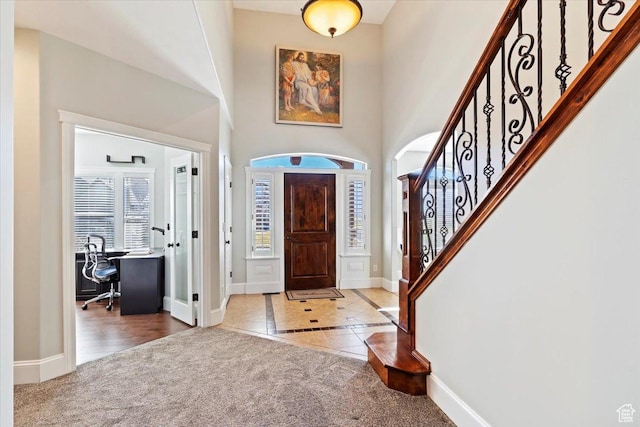 carpeted entryway featuring tile patterned flooring, a towering ceiling, baseboards, and stairs