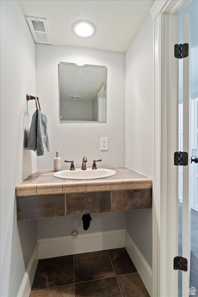 bathroom featuring baseboards, visible vents, a sink, and tile patterned floors