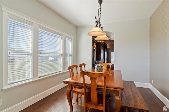 dining area with baseboards, wood finished floors, and arched walkways