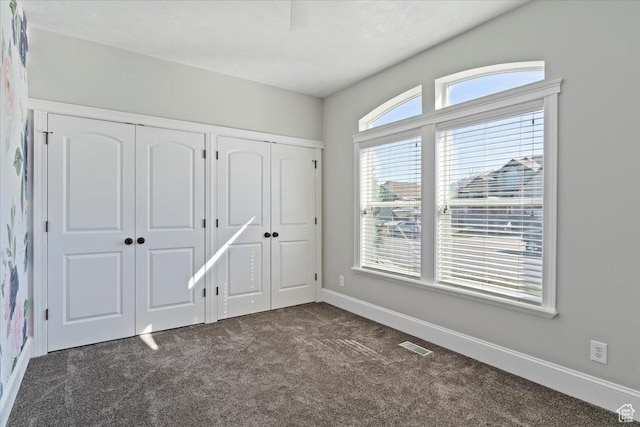 unfurnished bedroom with baseboards, multiple closets, visible vents, and dark carpet